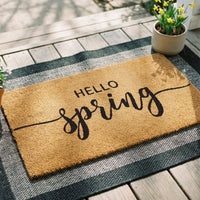 Hello Spring doormat in natural tan coir with script lettering, placed at [location context]