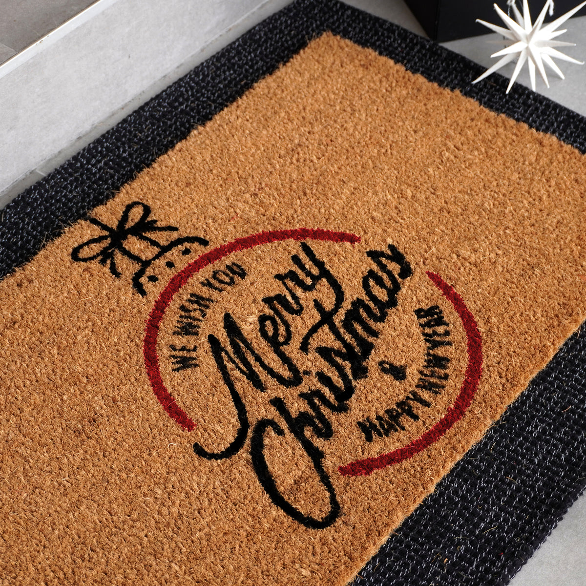 Christmas doormat featuring Merry Christmas script in circular design with decorative bow, natural coir fiber with red and bl