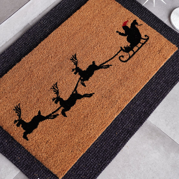 Sleigh natural coir doormat featuring Santa and reindeer silhouette in black and red, placed at [location/context]