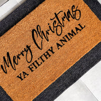 Natural coir doormat with 'Merry Christmas' in elegant script above 'Ya Filthy Animal' in bold block letters, photographed [a