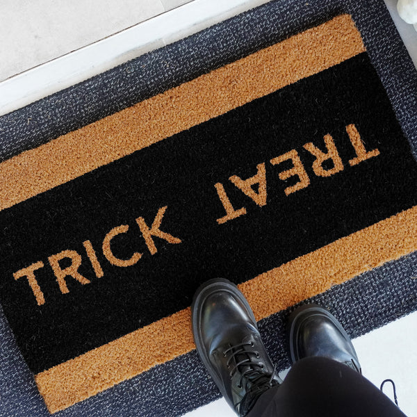 Trick or Treat Halloween doormat in natural coir with black center and natural border, shown [at front door/on porch/detail o